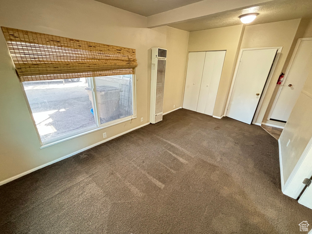 Unfurnished bedroom with a heating unit and dark colored carpet