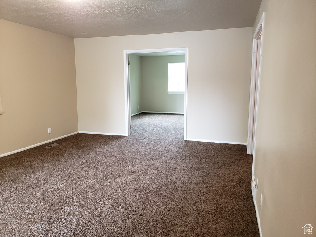 Empty room with dark colored carpet and a textured ceiling