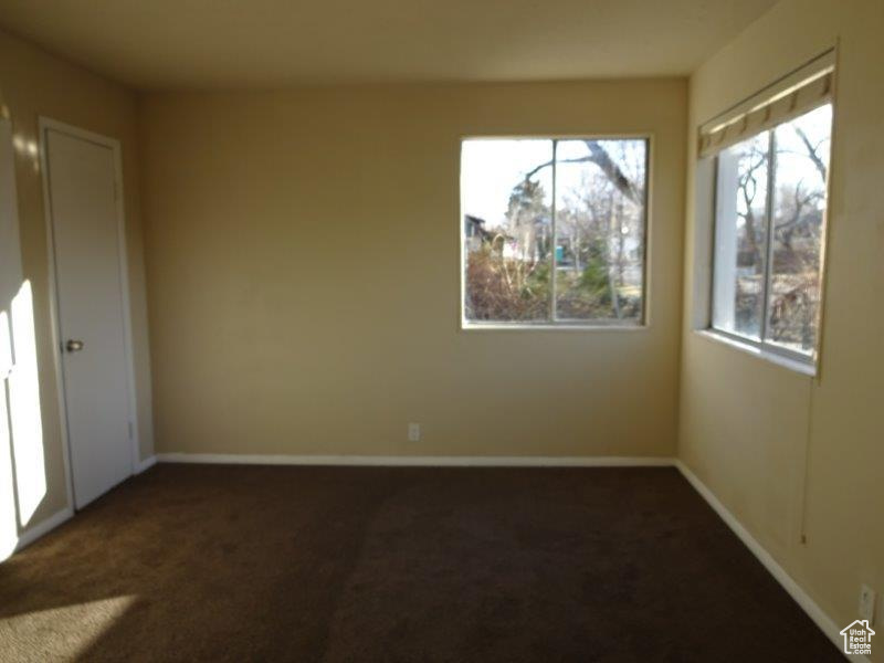 Unfurnished room with dark colored carpet and plenty of natural light
