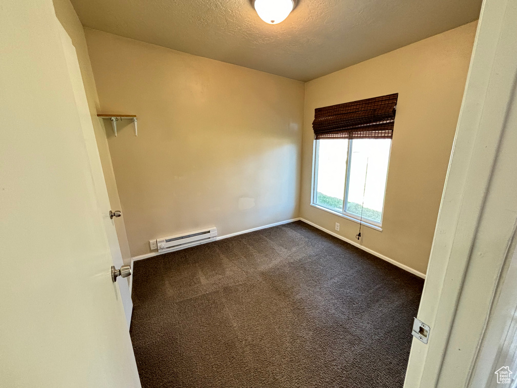 Unfurnished room featuring a baseboard radiator, dark colored carpet, and a textured ceiling