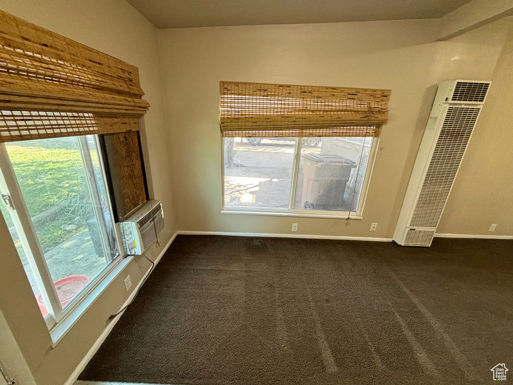 Unfurnished living room featuring a heating unit, dark carpet, and a wall mounted air conditioner