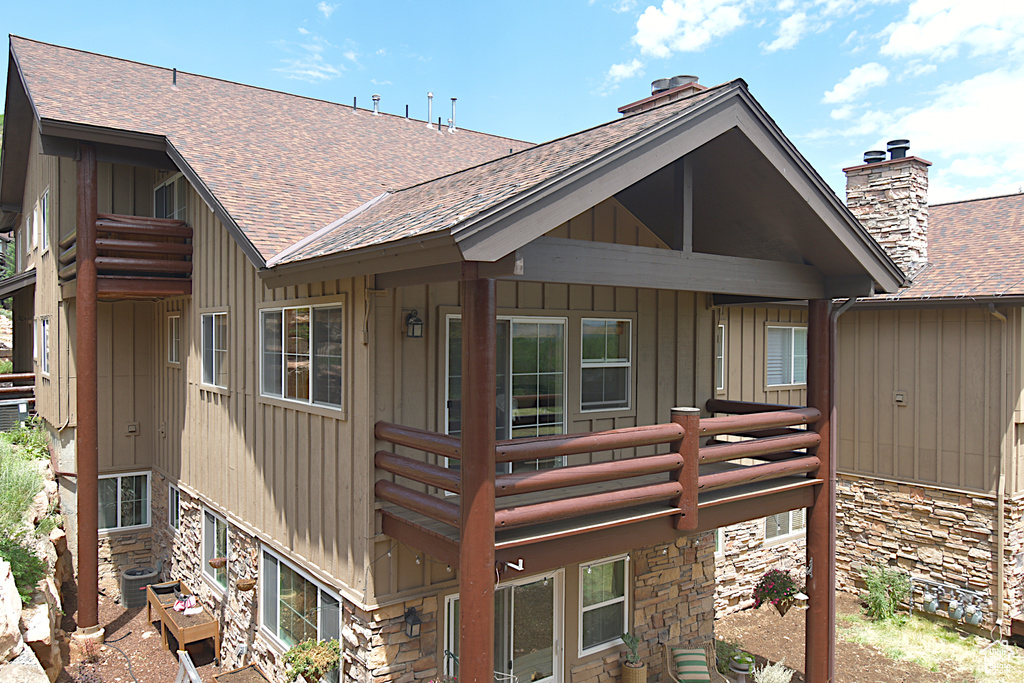 Back of property with a shingled roof, stone siding, board and batten siding, and a balcony