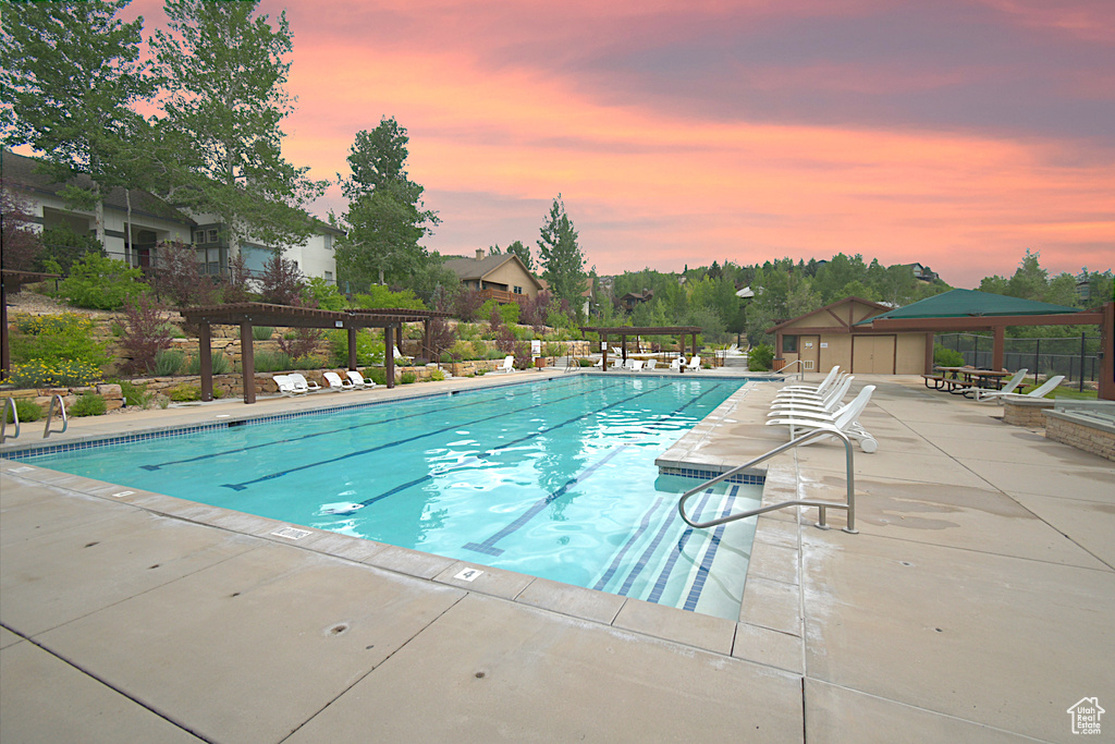 Pool at dusk with a pergola, a patio, and a community pool