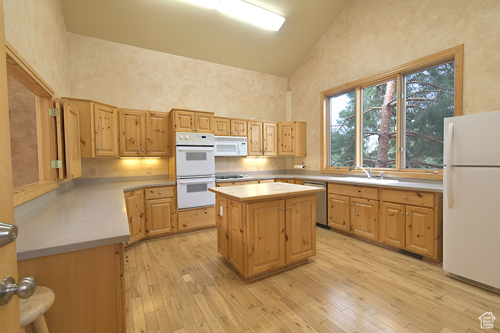 Kitchen featuring white appliances, high vaulted ceiling, light wood finished floors, tasteful backsplash, and light brown cabinets