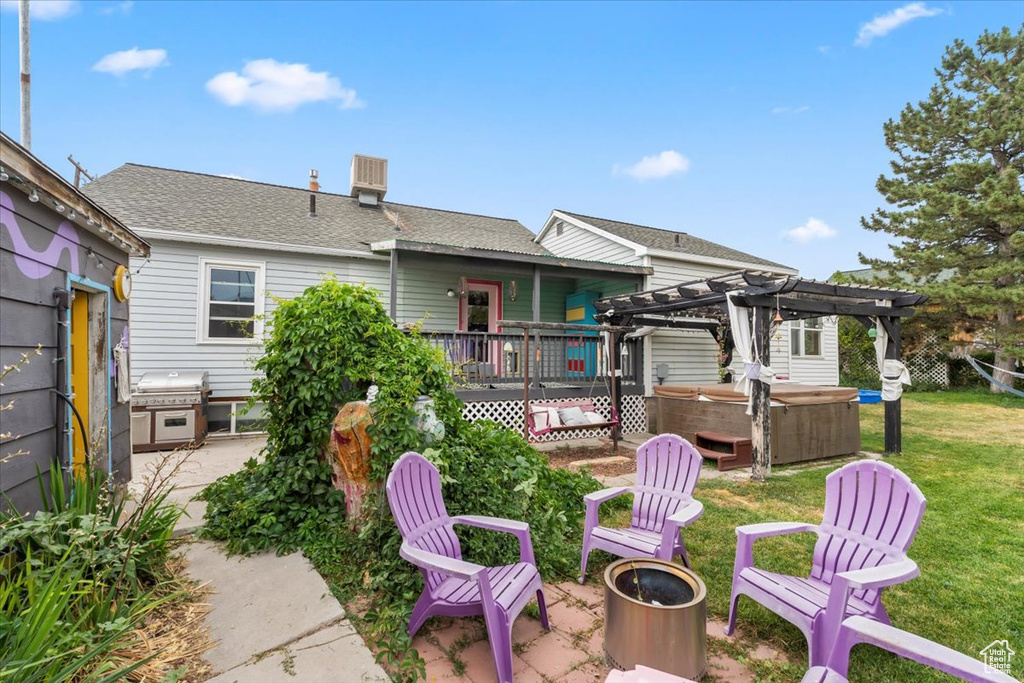 Rear view of property with a hot tub, a patio, a pergola, a fire pit, and a lawn