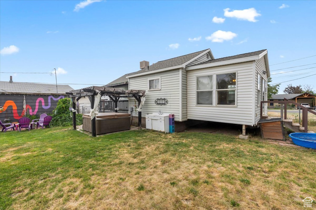 Back of house with a hot tub, a pergola, and a lawn