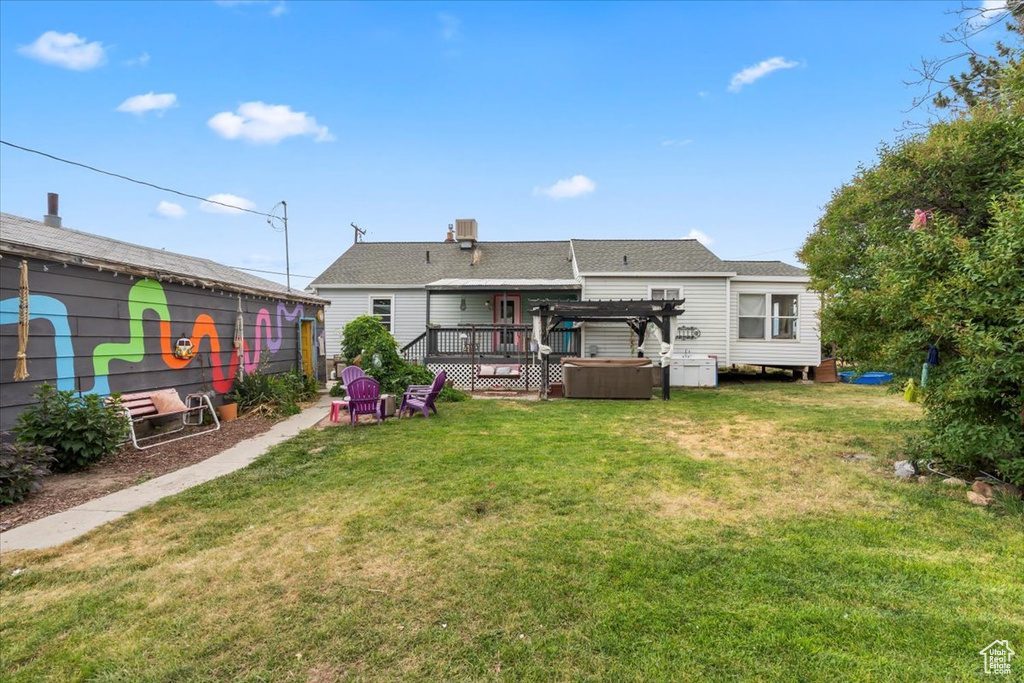 Rear view of property with a hot tub, a pergola, a lawn, and a deck