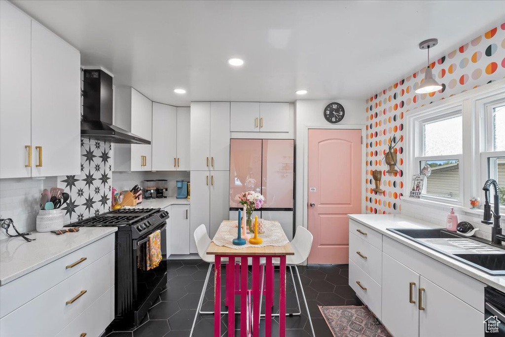 Kitchen with wall chimney range hood, black gas stove, white refrigerator, light countertops, and white cabinetry