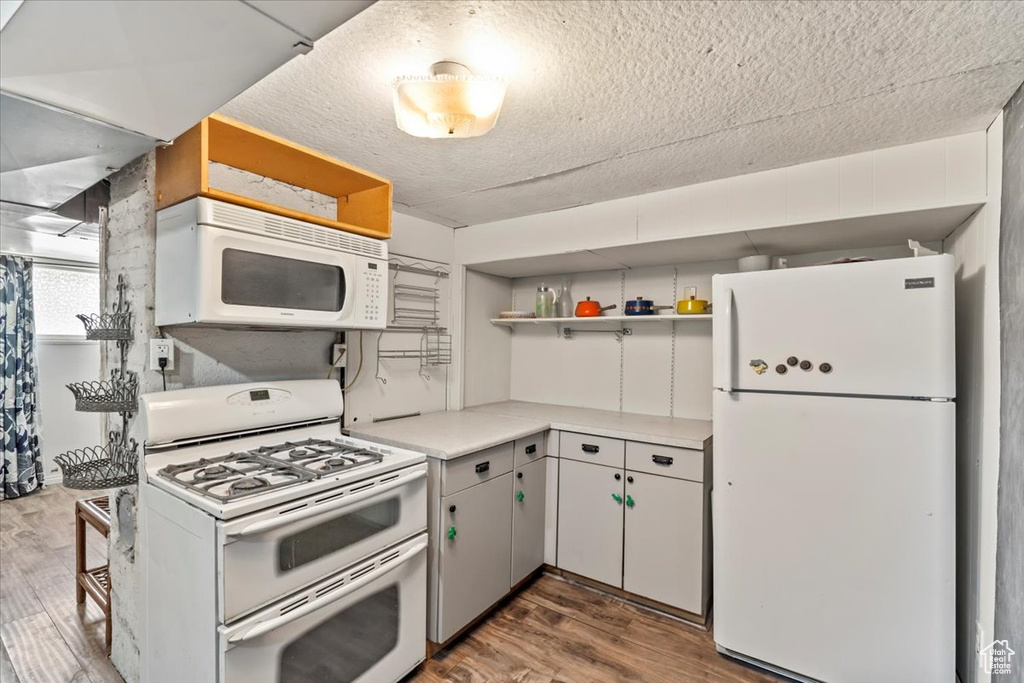 Kitchen with white appliances, open shelves, wood finished floors, light countertops, and a textured ceiling