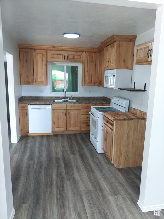 Kitchen featuring white appliances, dark countertops, and dark wood finished floors