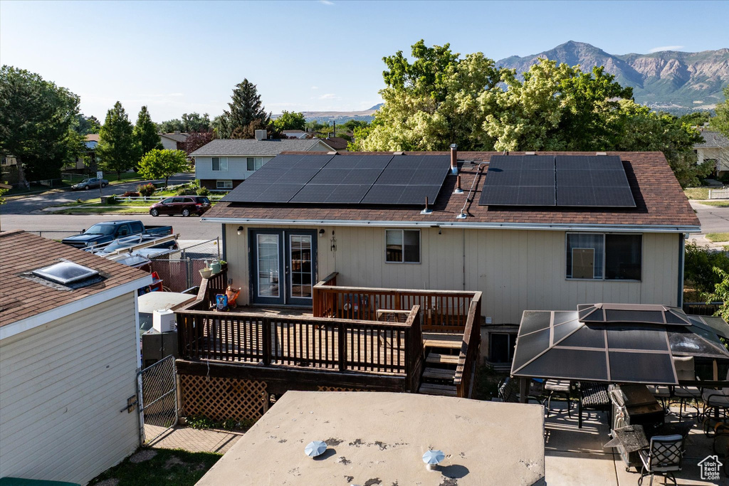 Rear view of house with a deck with mountain view, a shingled roof, solar panels, and outdoor dining area