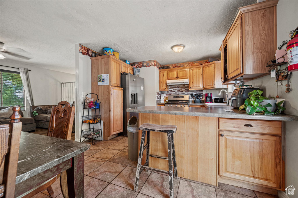 Kitchen with appliances with stainless steel finishes, under cabinet range hood, a peninsula, a textured ceiling, and light tile patterned flooring