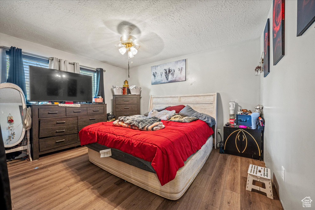 Bedroom with a textured ceiling, wood finished floors, and a ceiling fan