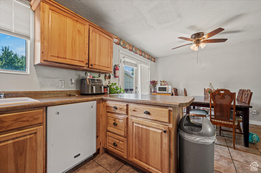 Kitchen with plenty of natural light, a ceiling fan, a peninsula, white appliances, and a textured ceiling
