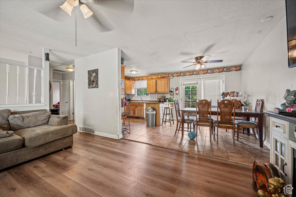Living room featuring a ceiling fan, a textured ceiling, and light wood finished floors