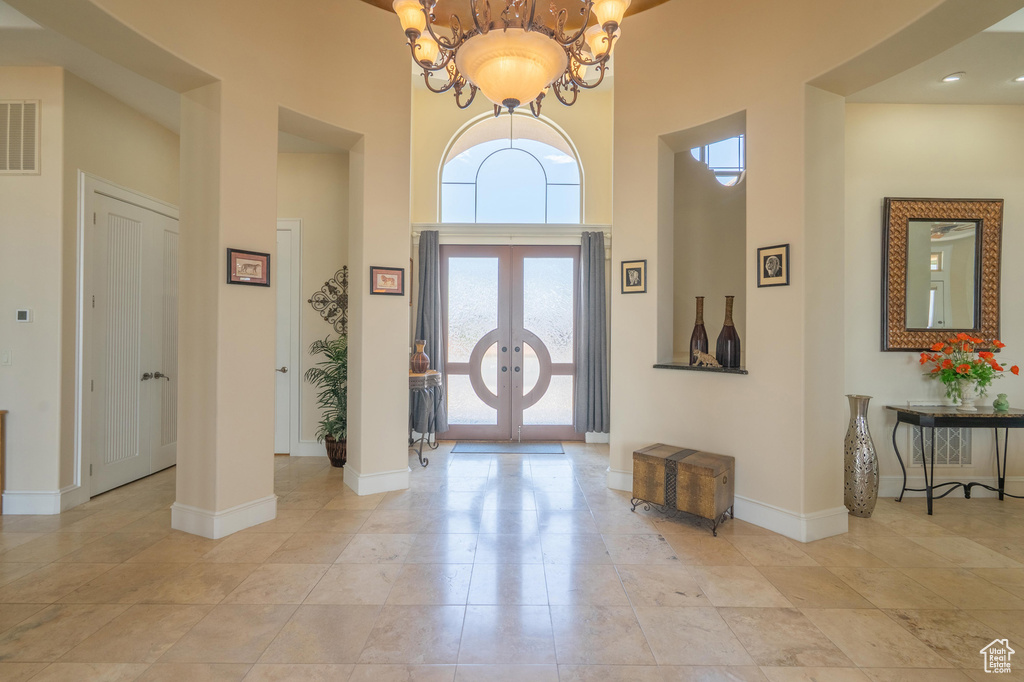 Entryway with a high ceiling, french doors, a chandelier, and light tile patterned floors