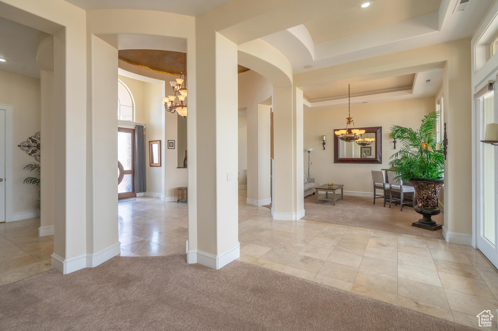 Foyer entrance with a chandelier, arched walkways, a tray ceiling, light tile patterned floors, and light colored carpet