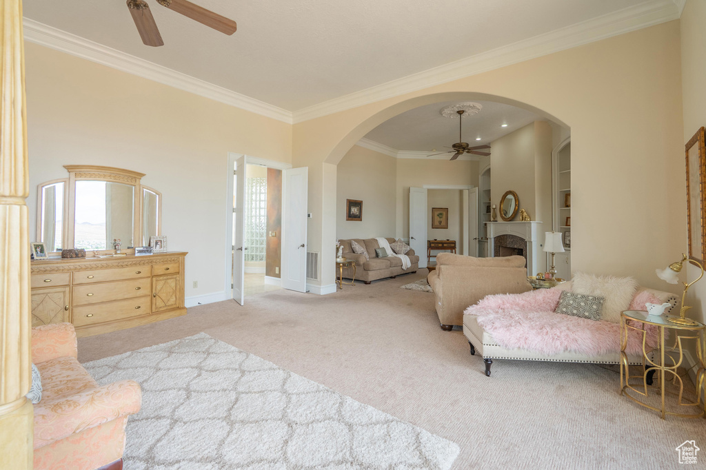 Carpeted bedroom with crown molding, arched walkways, a fireplace, and a ceiling fan