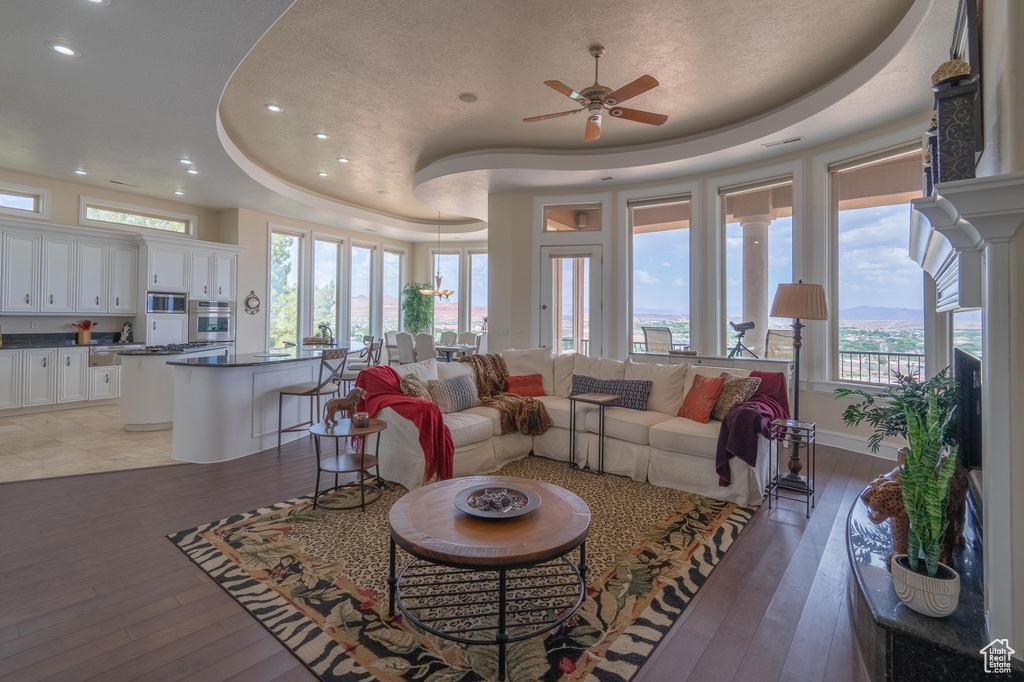 Living area with a raised ceiling, a ceiling fan, recessed lighting, light wood finished floors, and healthy amount of natural light