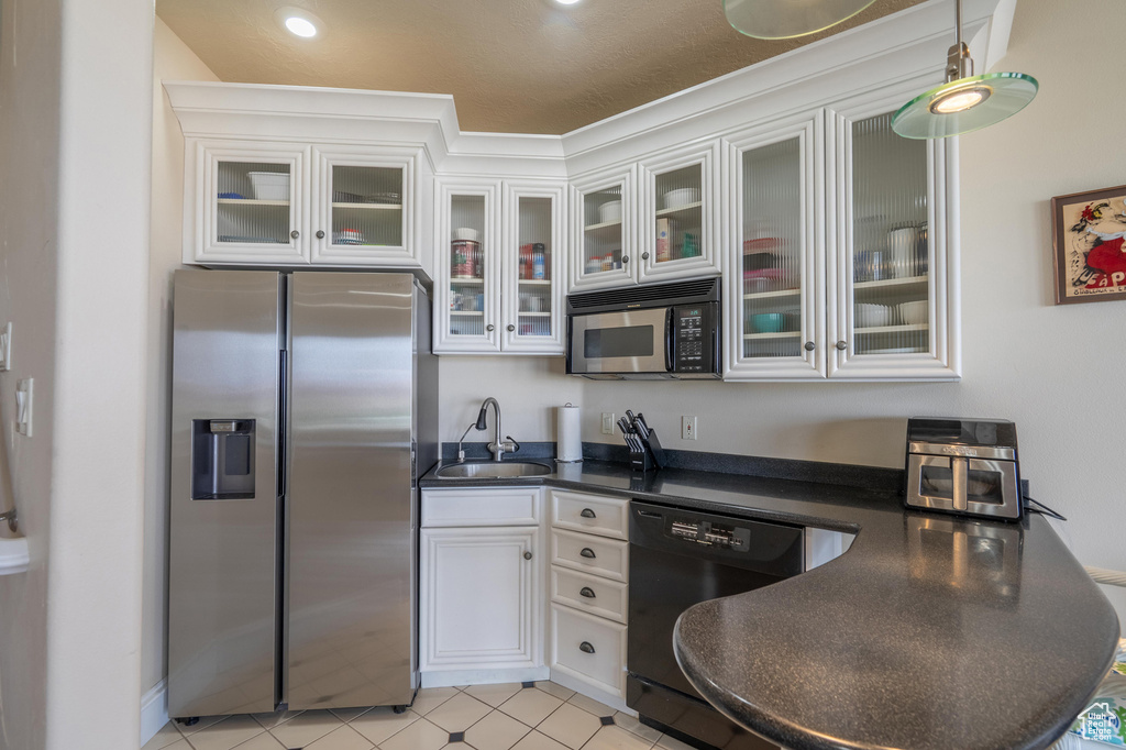Kitchen featuring stainless steel refrigerator with ice dispenser, black dishwasher, dark countertops, white cabinetry, and glass insert cabinets
