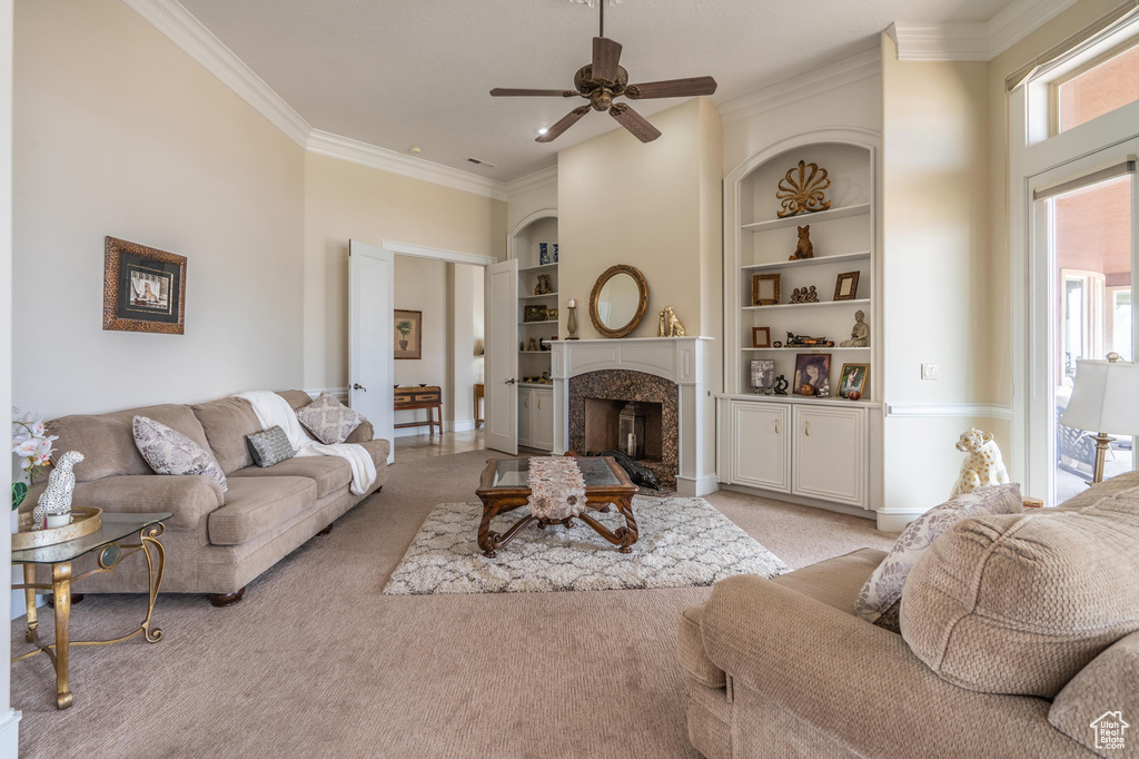 Living area featuring light colored carpet, ornamental molding, a premium fireplace, built in features, and a ceiling fan