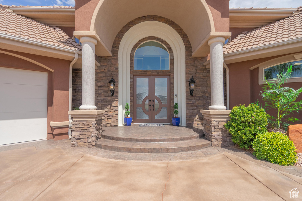 Property entrance featuring a tile roof, stucco siding, stone siding, a garage, and driveway
