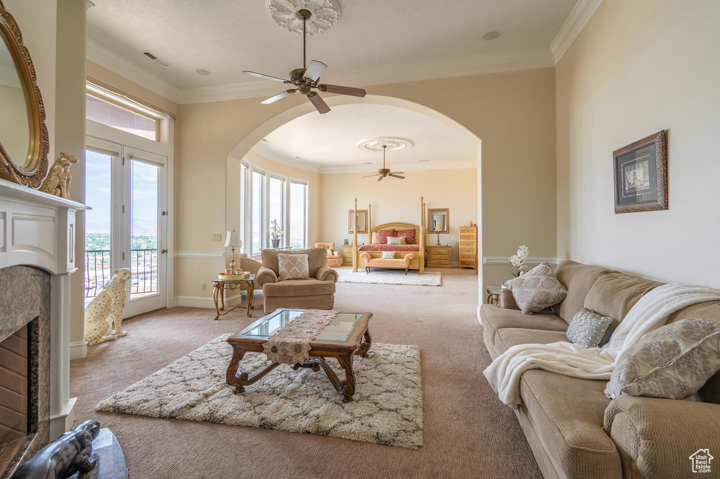 Carpeted living room featuring arched walkways, ceiling fan, plenty of natural light, and ornamental molding