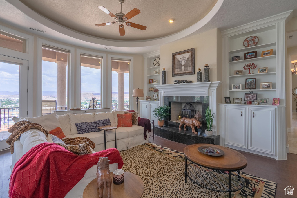 Living room featuring built in features, ceiling fan, a fireplace, wood finished floors, and a raised ceiling