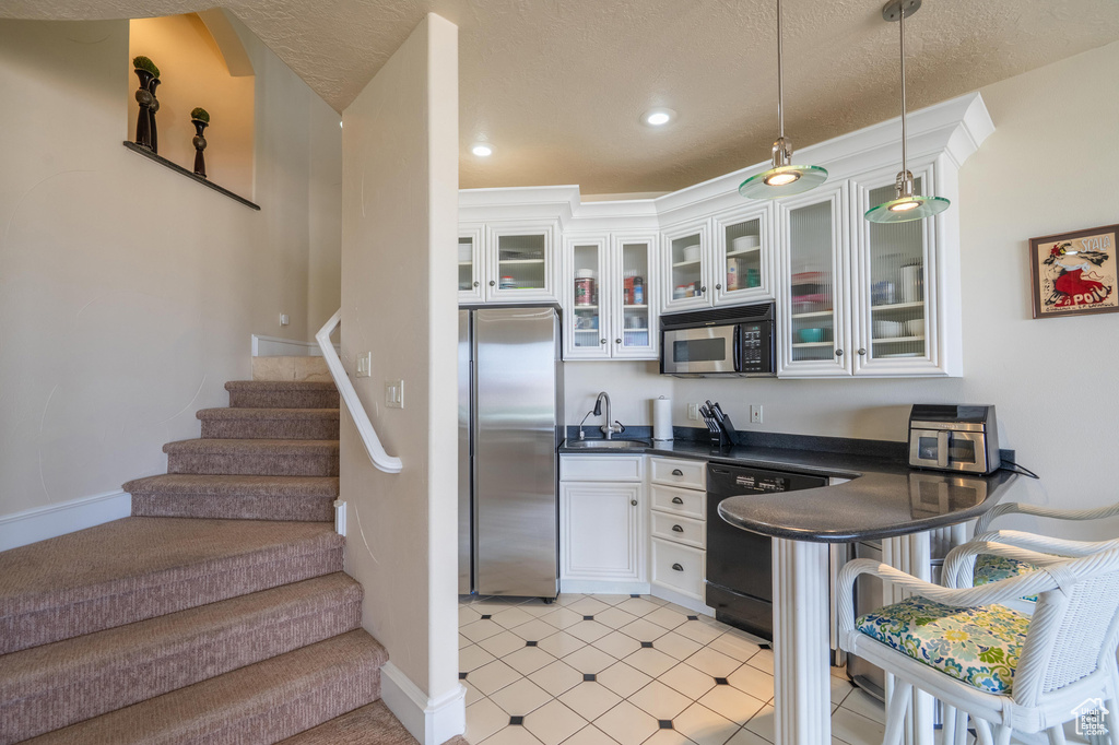 Kitchen with freestanding refrigerator, dark countertops, white cabinetry, dishwashing machine, and pendant lighting