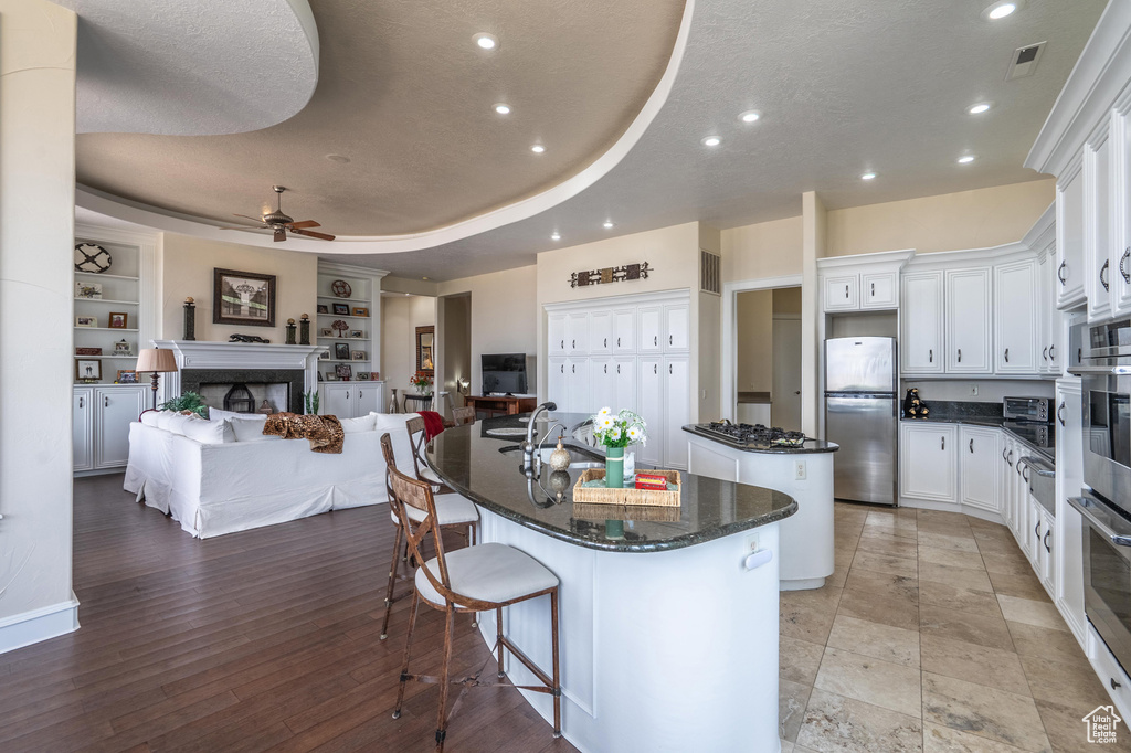Kitchen featuring freestanding refrigerator, an island with sink, a fireplace, ceiling fan, and open floor plan