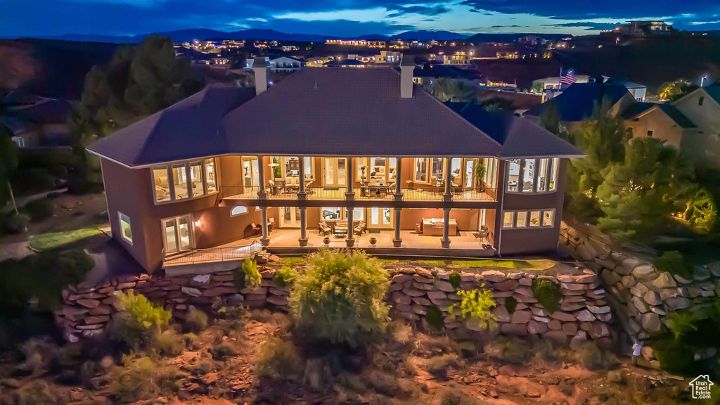 Back of house at night with a balcony, a chimney, and a patio area