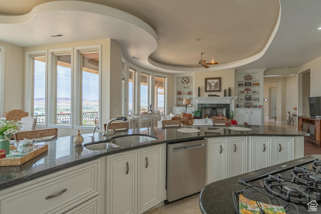 Kitchen with stainless steel dishwasher, open floor plan, built in shelves, a fireplace, and dark stone countertops