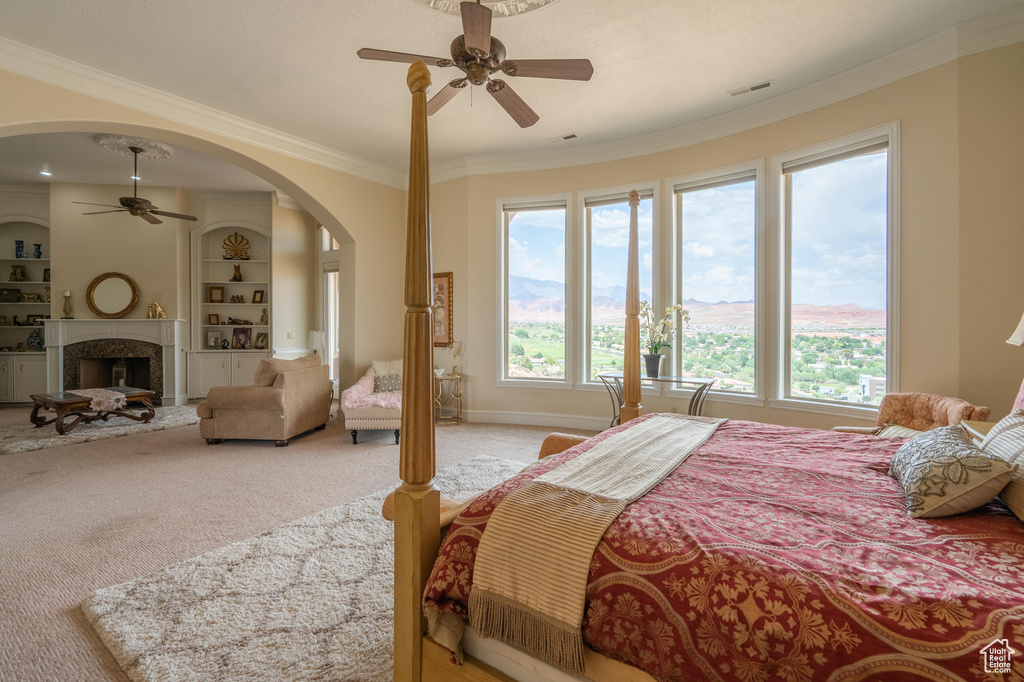 Bedroom with ornamental molding, multiple windows, light carpet, arched walkways, and a high end fireplace
