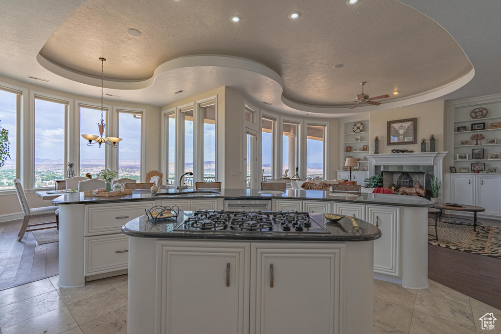 Kitchen with gas stovetop, a tray ceiling, a center island, built in shelves, and a ceiling fan