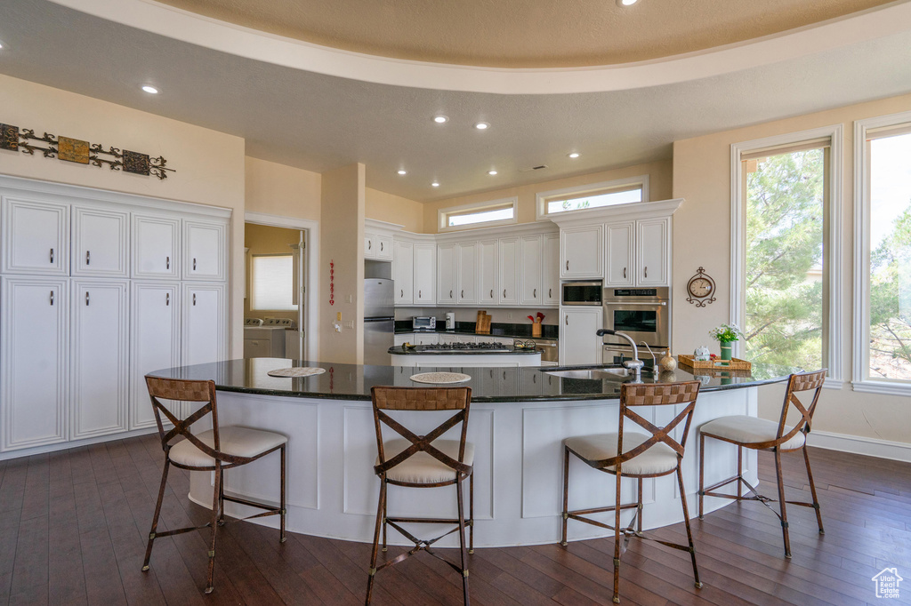 Kitchen featuring stainless steel appliances, white cabinetry, dark wood-type flooring, recessed lighting, and a kitchen breakfast bar