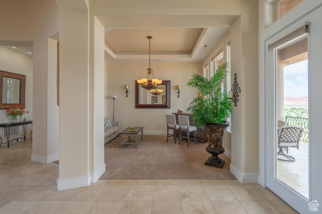 Entrance foyer featuring a chandelier, light carpet, a tray ceiling, and light tile patterned floors