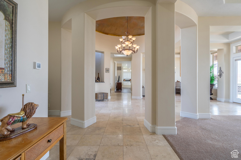 Corridor featuring arched walkways, a chandelier, ornate columns, and light carpet