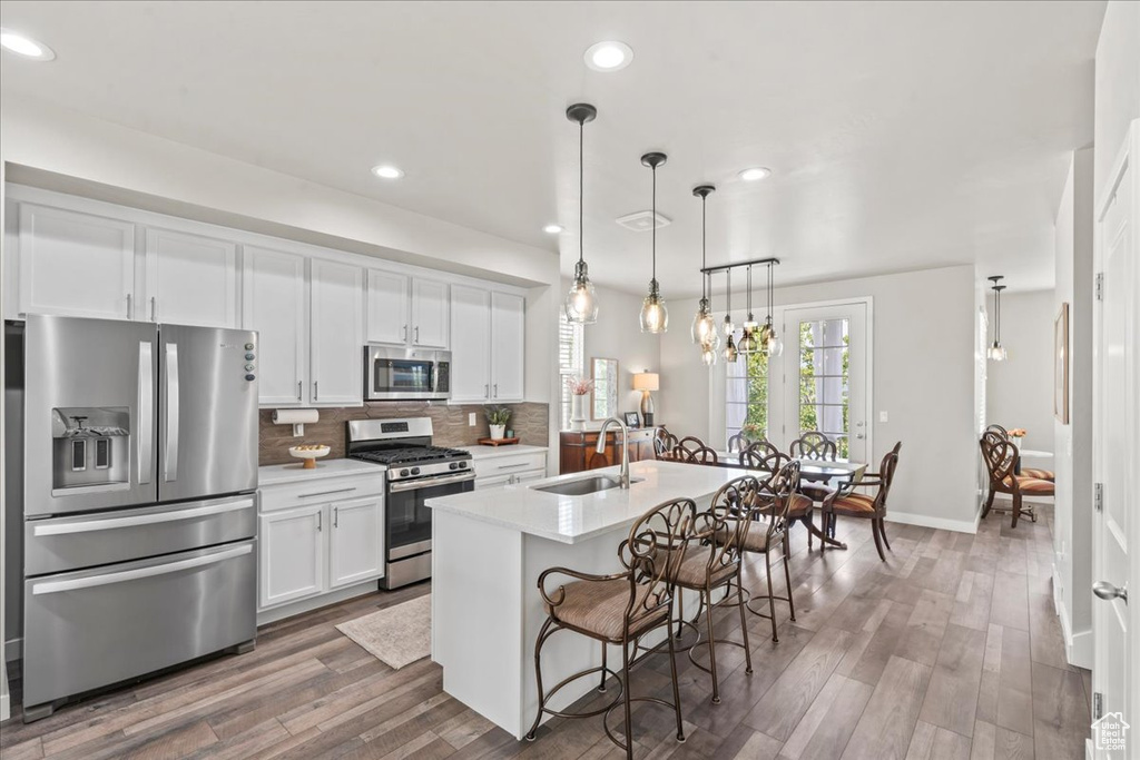 Kitchen with stainless steel appliances, tasteful backsplash, light countertops, white cabinetry, and wood finished floors