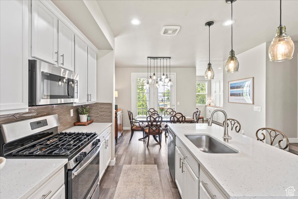 Kitchen with appliances with stainless steel finishes, dark wood-style floors, a center island with sink, white cabinets, and decorative backsplash