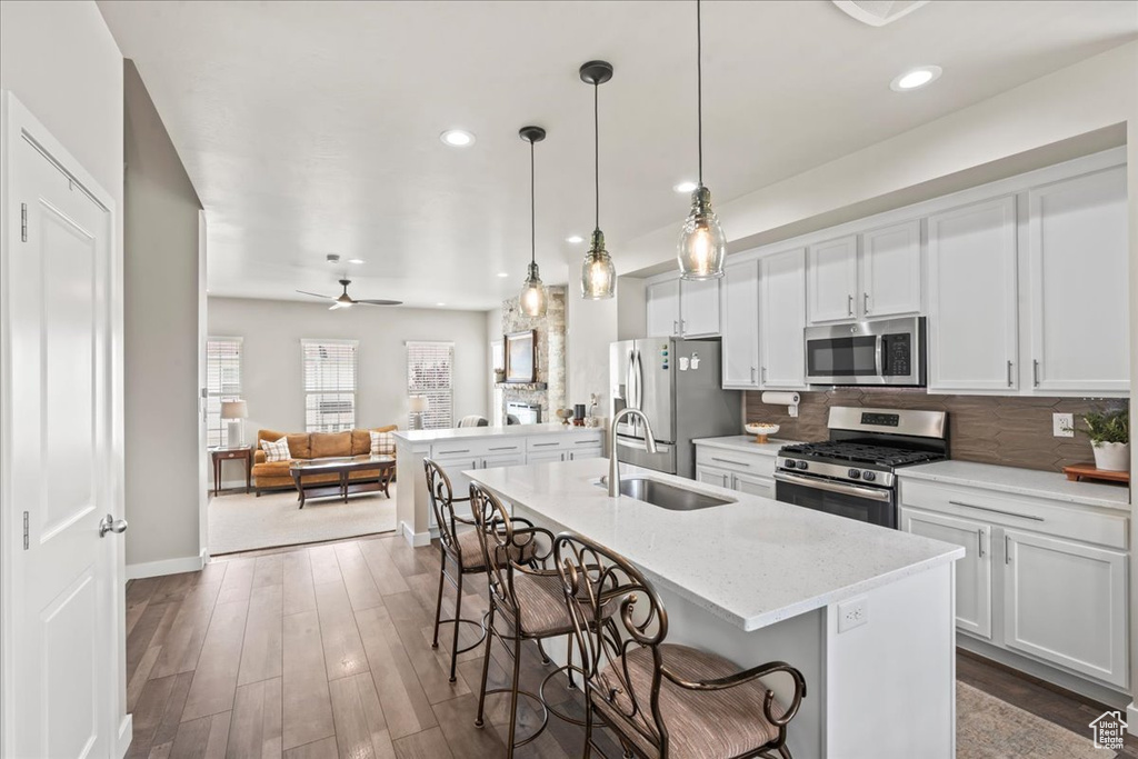 Kitchen with appliances with stainless steel finishes, a breakfast bar area, a kitchen island with sink, open floor plan, and decorative backsplash