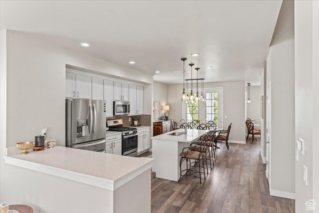 Kitchen featuring stainless steel appliances, a breakfast bar, white cabinetry, tasteful backsplash, and wood finished floors