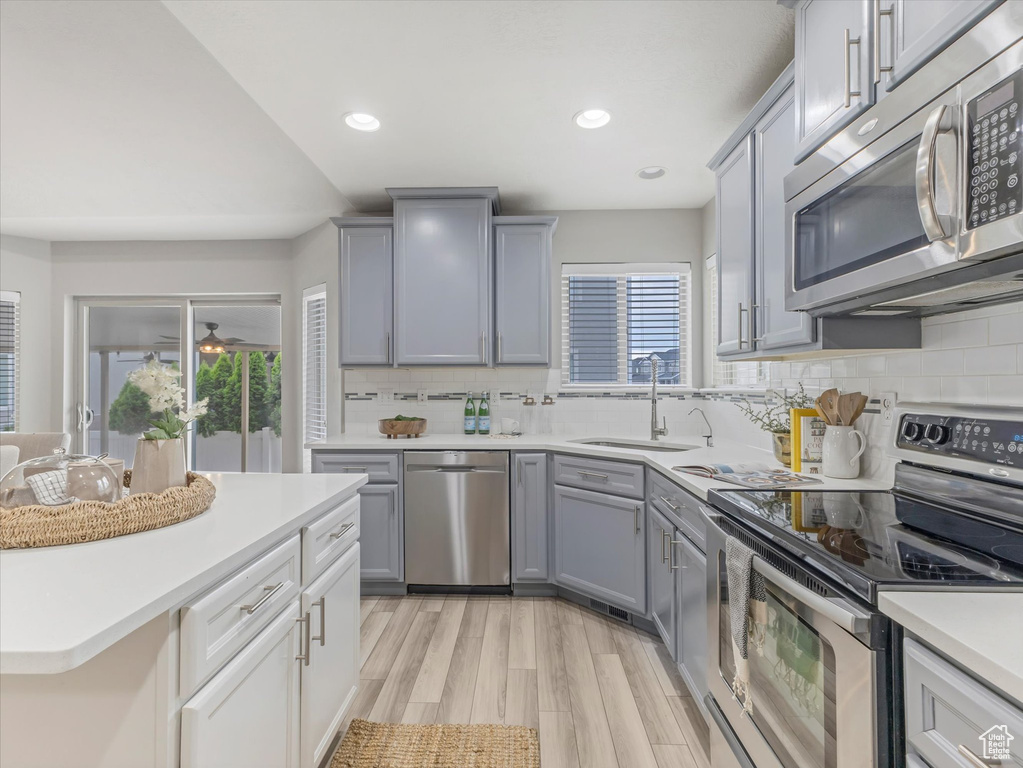 Kitchen with appliances with stainless steel finishes, gray cabinets, light countertops, tasteful backsplash, and recessed lighting