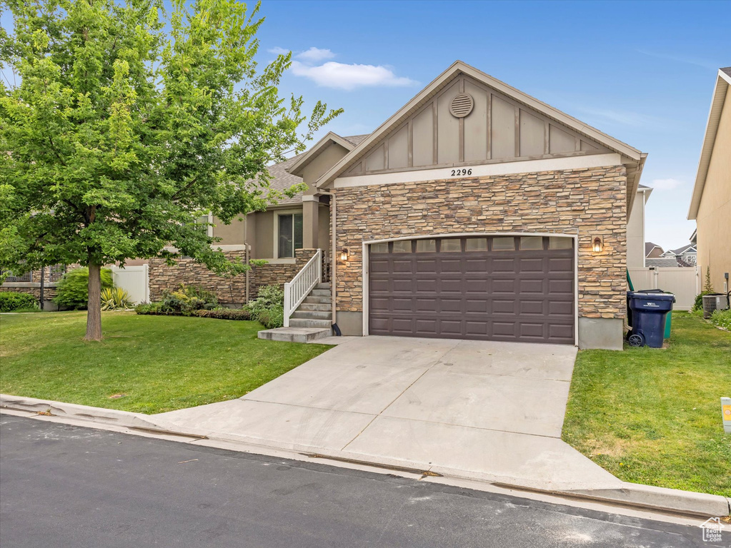 View of front of house featuring stone siding, board and batten siding, a front lawn, and concrete driveway