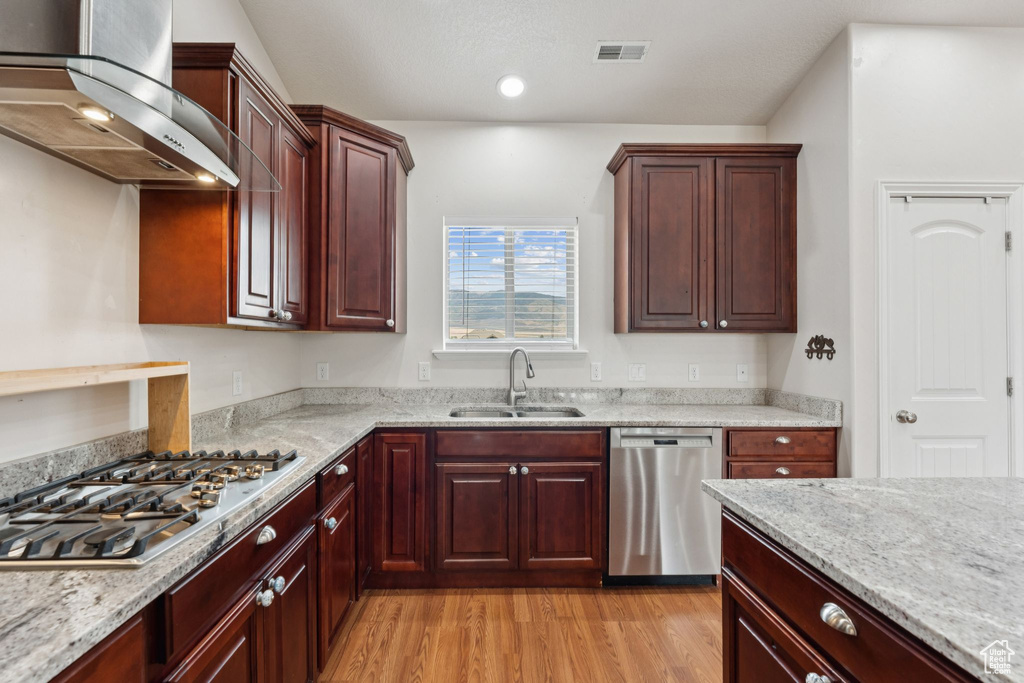 Kitchen with wall chimney exhaust hood, appliances with stainless steel finishes, light wood finished floors, and light stone countertops