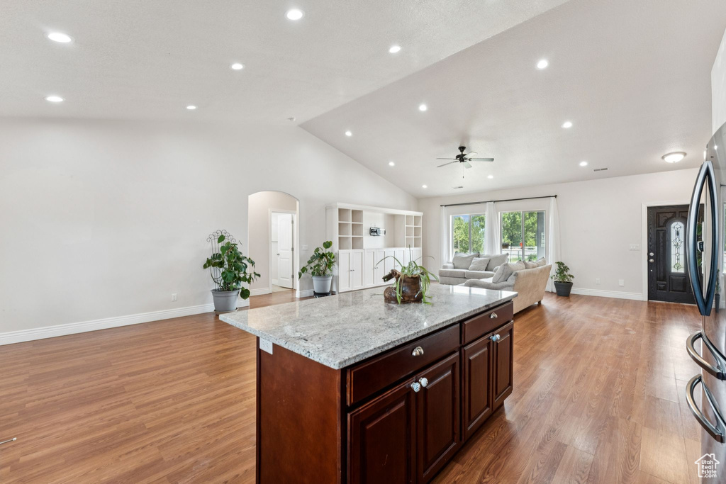 Kitchen featuring open floor plan, a ceiling fan, arched walkways, light stone counters, and light wood-style floors
