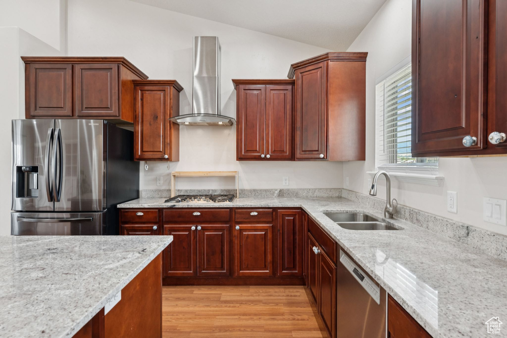 Kitchen with stainless steel appliances, wall chimney range hood, lofted ceiling, light stone countertops, and light wood finished floors