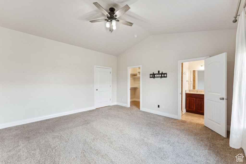 Unfurnished bedroom with vaulted ceiling, light carpet, a spacious closet, a closet, and ceiling fan