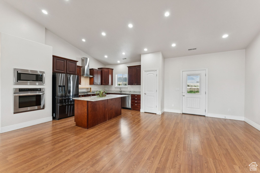 Kitchen with stainless steel appliances, wall chimney range hood, a center island, light wood-type flooring, and dark brown cabinetry