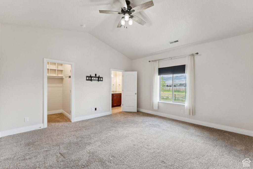 Unfurnished bedroom featuring light colored carpet, lofted ceiling, a spacious closet, ceiling fan, and a closet