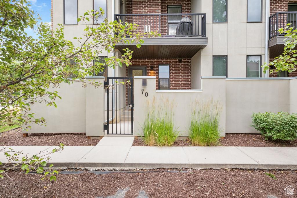 View of exterior entry with a balcony, a gate, brick siding, and stucco siding